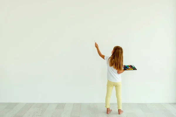 Little girl painting on white wall indoors — Stock Photo, Image