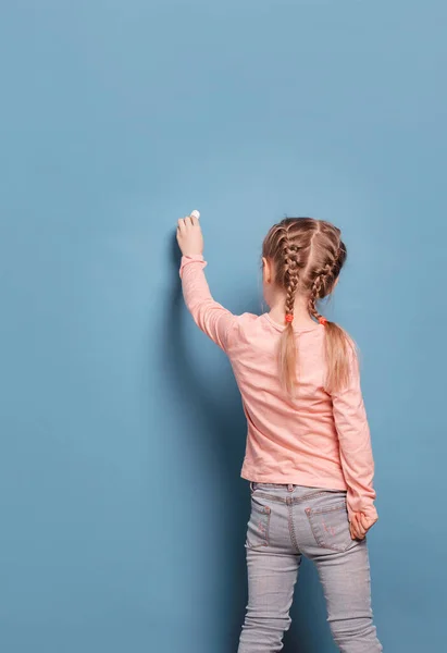 Kleines Mädchen schreibt mit Kreide auf blauem Hintergrund — Stockfoto
