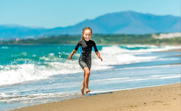 Girl in a wetsuit running along the beach — Stock Photo, Image