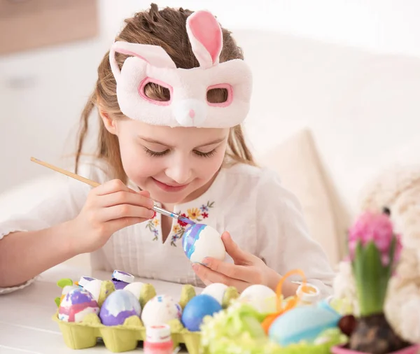 Girl coloring eggs in mask — Stock Photo, Image