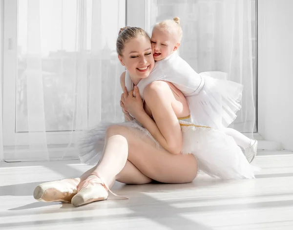 Giovane madre che abbraccia piccola figlia sorridente in studio di danza classica — Foto Stock