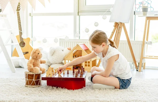Pieni tyttö pelaa shakkia teddyn kanssa — kuvapankkivalokuva