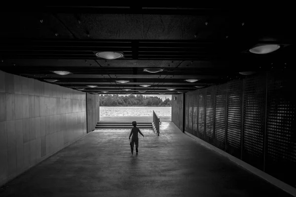 Lonely young boy with umbrella in long tunnel walkway with the white light at the end