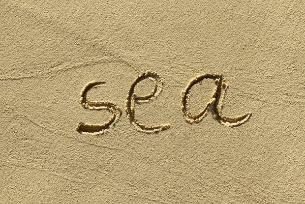 Натуральный песочный фон с нацарапанным словом "море" — стоковое фото