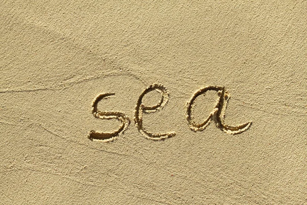 Натуральный песочный фон с нацарапанным словом "море" — стоковое фото