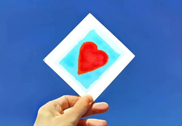 Hand hält ein Bild eines Herzens gegen den blauen Himmel — Stockfoto