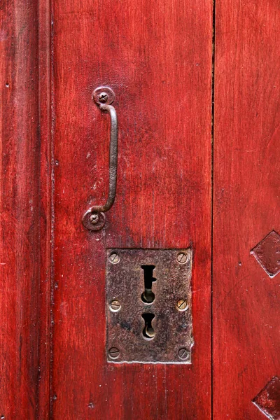 Vintage red wooden door with metallic handle and keyholes — Stock Photo, Image