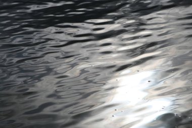 Dalgalı su yüzeyinde güneş parlıyor.