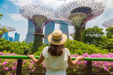 SINGAPORE - 23 Haziran 2019: Beyaz elbiseli ve hasır şapkalı kadın gezgin Singapur 'daki Marina Körfezi Kumları ve Bahçeleri' ne bakıyor