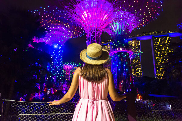 SINGAPORE, SINGAPORE - FEBRUARY 26, 2020: Woman traveler looking at Gardens by the Bay and Marina Bay Sands Hotel at night in Singapore