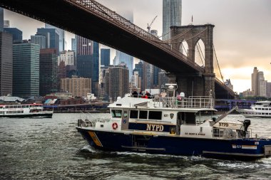 NEW YORK CITY, ABD - 15 Mart 2020: Brooklyn Köprüsü 'nde NYPD polis botu ve New York City, ABD' de günbatımından sonra Manhattan şehir merkezinin panoramik gün batımı görüntüsü