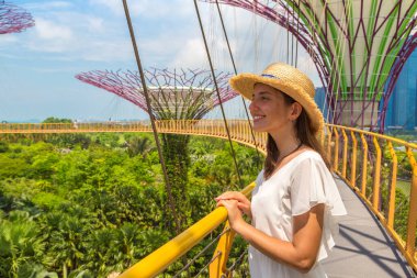 SINGAPORE - 23 Haziran 2019 Singapur Körfezi yakınlarındaki Gardens 'taki Skyway Köprüsü' nde beyaz elbise ve hasır şapka giyen kadın gezgin