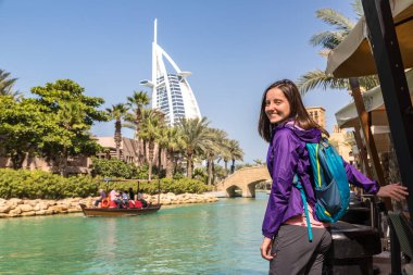 DUBAI, BİRLİK ARAB EMIRATES - 31 Ocak 2020: Burj Al Arap Oteli ve Dubai 'deki Madinat Jumeirah Oteli yakınlarında yürüyen mutlu kız gezgin