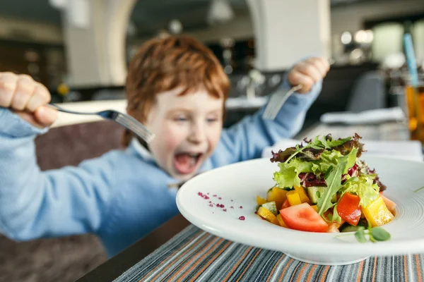 Niño pelirrojo con tenedores comiendo ensalada Imagen de archivo