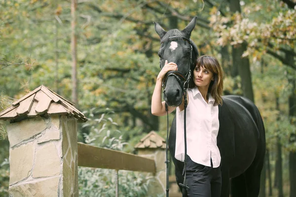 Portret van de jonge vrouw en zwarte paard in een bos. — Stockfoto