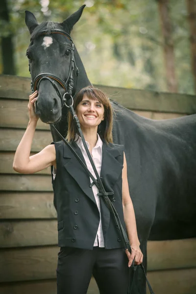 Portret młodej kobiety i czarnego konia w lesie. — Zdjęcie stockowe