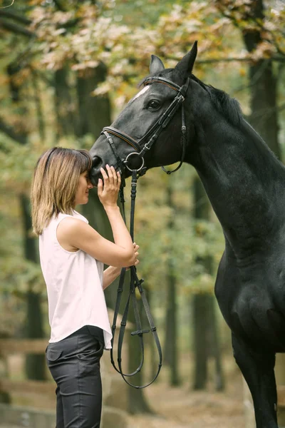 Portret van de jonge vrouw en zwarte paard in een bos. — Stockfoto