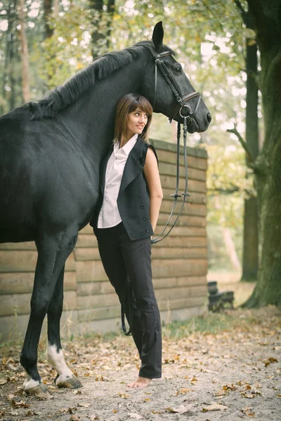 Portret van de jonge vrouw en zwarte paard in een bos. — Stockfoto