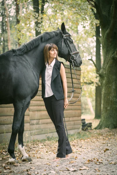 Portret van de jonge vrouw en zwarte paard in een bos. — Stockfoto