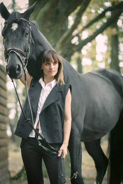 Portret van de jonge vrouw en zwarte paard in een bos. — Stockfoto