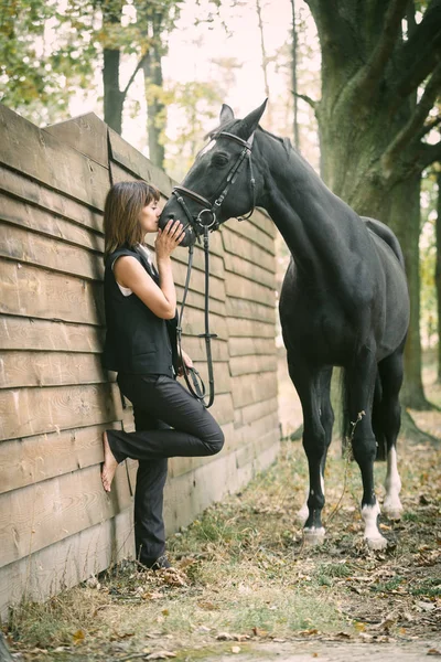 Portret van de jonge vrouw en zwarte paard in een bos. — Stockfoto