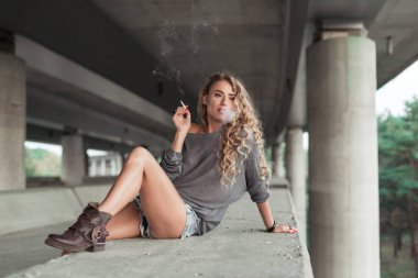 Güzel kıvırcık genç kadın bir sanayi üzerinde lo Sigara