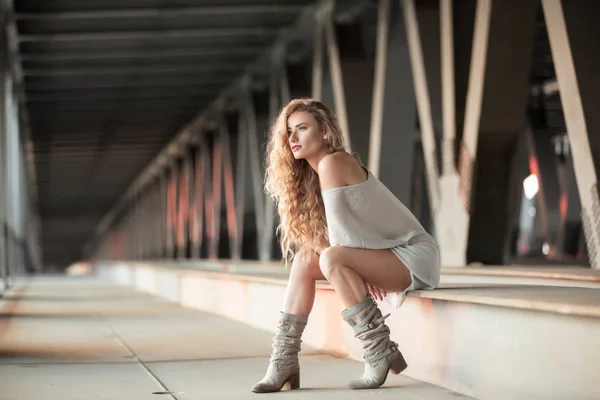 Beautiful curly young woman sitting on industrial bridge locatio