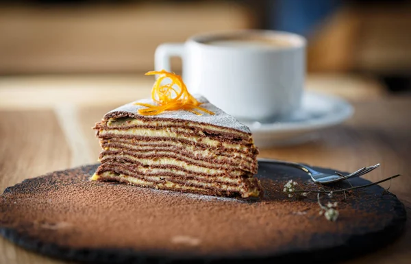 Piece of cacao sliced cake on a slate round plate with a cup of — Stock Photo, Image