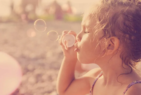 Cinco años de edad hermosa niña sopla burbujas de jabón en un sol —  Fotos de Stock