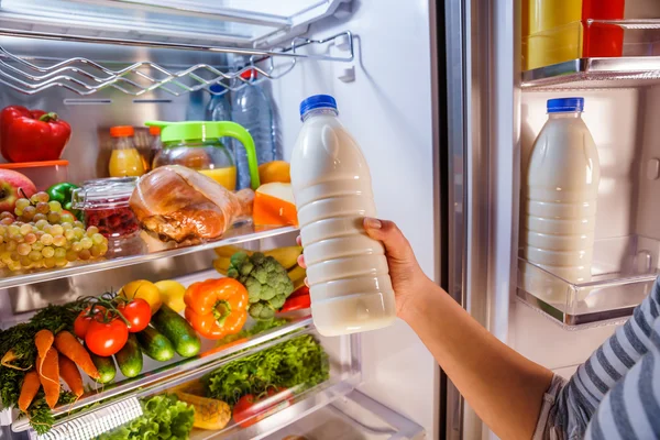 La mujer toma la leche del refrigerador abierto — Foto de Stock