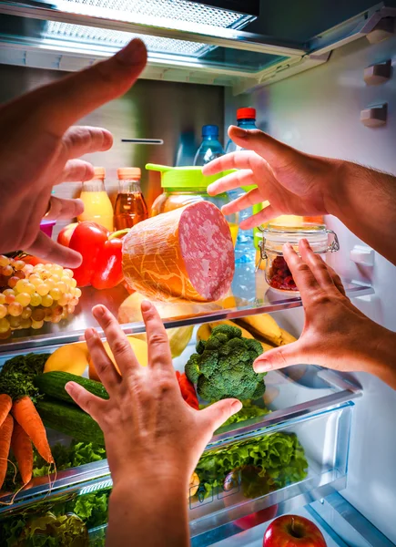 Human hands reaching for food at night in the open refrigerator — Stock Photo, Image