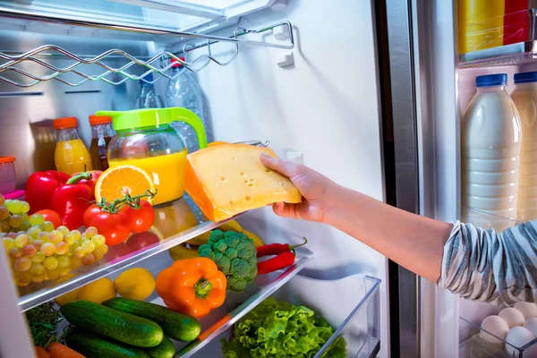 Frau holt das Stück Käse aus dem offenen Kühlschrank — Stockfoto