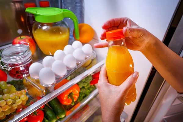 Kvinna tar apelsinjuice från öppna kylskåpet — Stockfoto