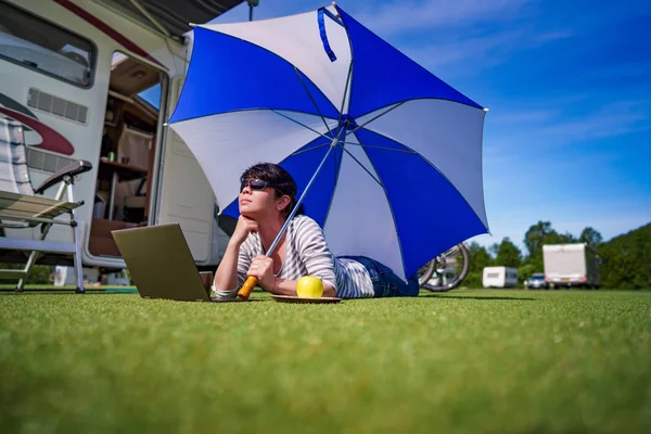 Mujer en la hierba, mirando el portátil bajo el paraguas cerca de th — Foto de Stock