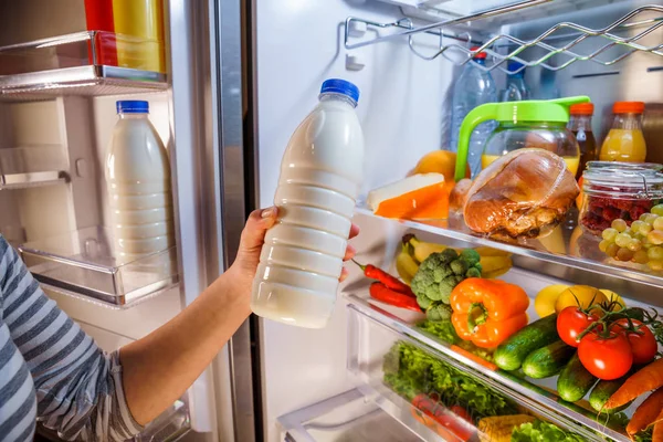 Woman takes the milk from the open refrigerator — Stock Photo, Image