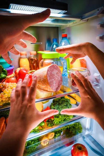 Руки людини досягають їжі вночі у відкритому холодильнику — стокове фото