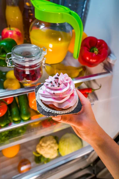 Женщина берет сладкий торт из открытого холодильника — стоковое фото