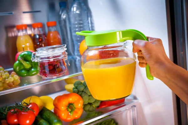 Mulher tira o suco de laranja da geladeira aberta — Fotografia de Stock