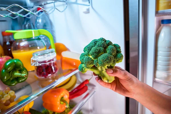 La donna prende i broccoli dal frigorifero aperto . — Foto Stock