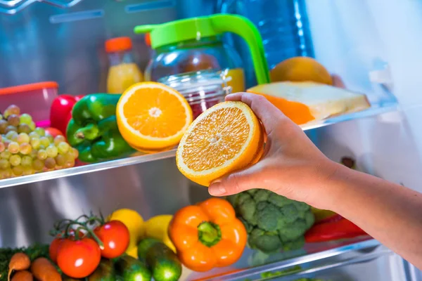 Mulher tira a laranja da geladeira aberta . — Fotografia de Stock
