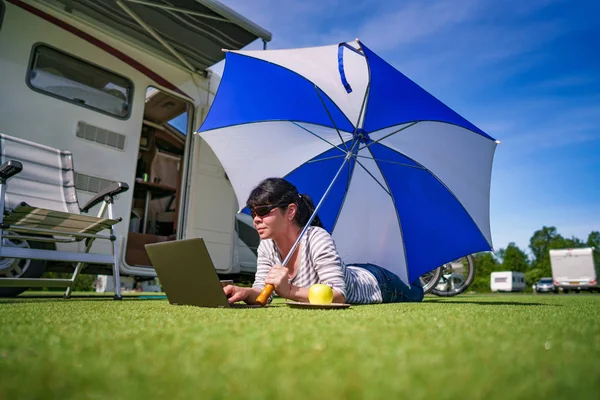 Mujer en la hierba, mirando el portátil bajo el paraguas cerca de th — Foto de Stock