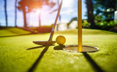 Gün batımında deliğin yanında sopayla birlikte mini golf topu.