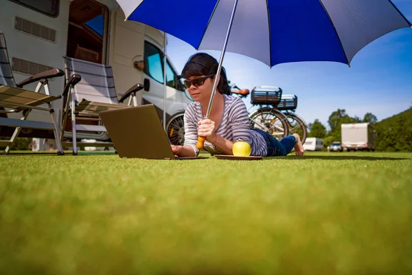 Женщина на траве, глядя на ноутбук под зонтиком рядом с й — стоковое фото