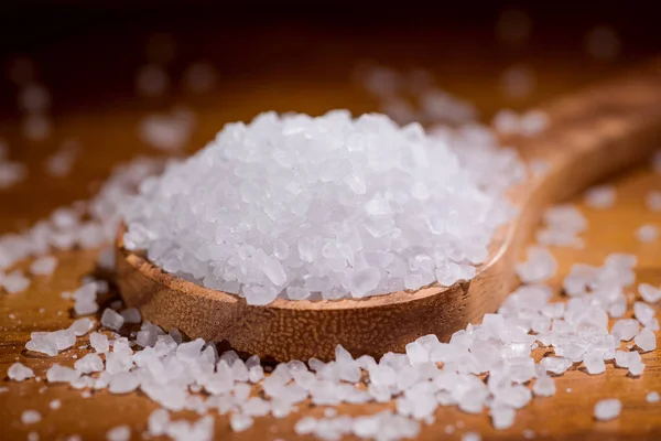 Sea salt crystals closeup in wooden spoon on a kitchen table. — Stock Photo, Image