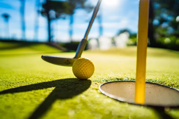 Mini Golf gele bal met een knuppel bij het gat bij zonsondergang — Stockfoto