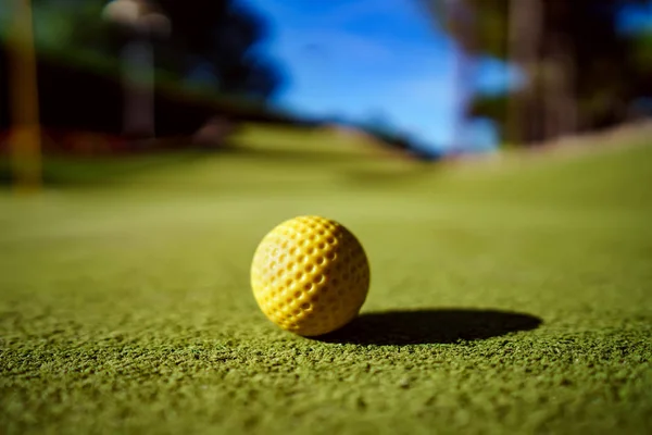 Мини гольф желтый мяч на зеленой траве на закате — стоковое фото