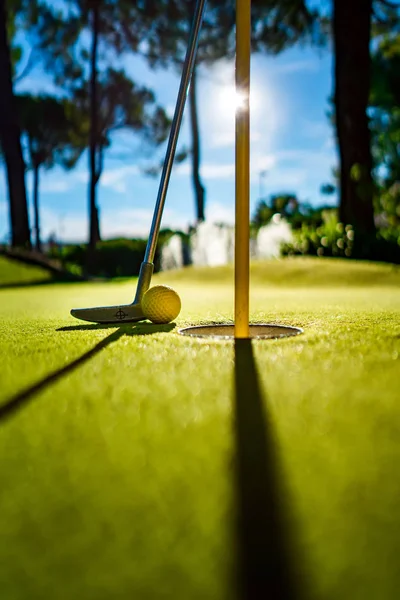 Mini balle jaune golf avec une chauve-souris près du trou au coucher du soleil — Photo