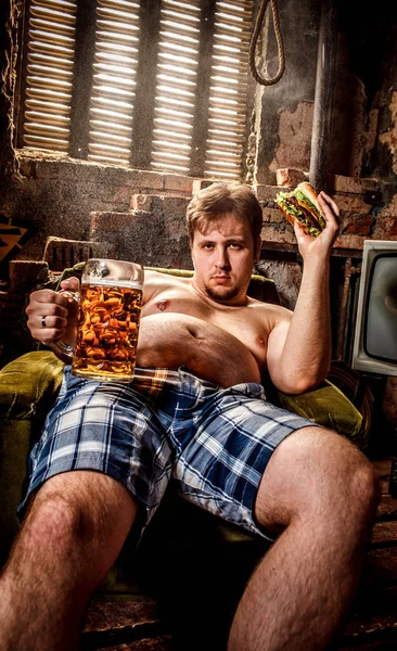 Dikke man eten van een hamburger zittend op een stoel in de sloppenwijken — Stockfoto