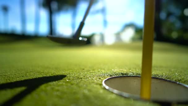 Gün batımında deliğin yanında sopayla birlikte mini golf topu. — Stok video
