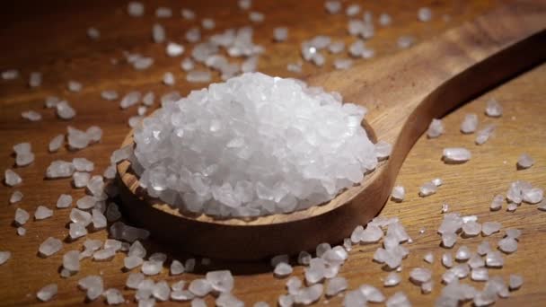 Kryształy soli morskiej zbliżenie w drewnianej łyżce na stole kuchennym. — Wideo stockowe